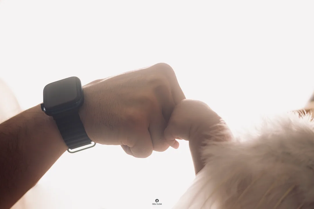 A baby's hand holding on to a father's fist in soft white light