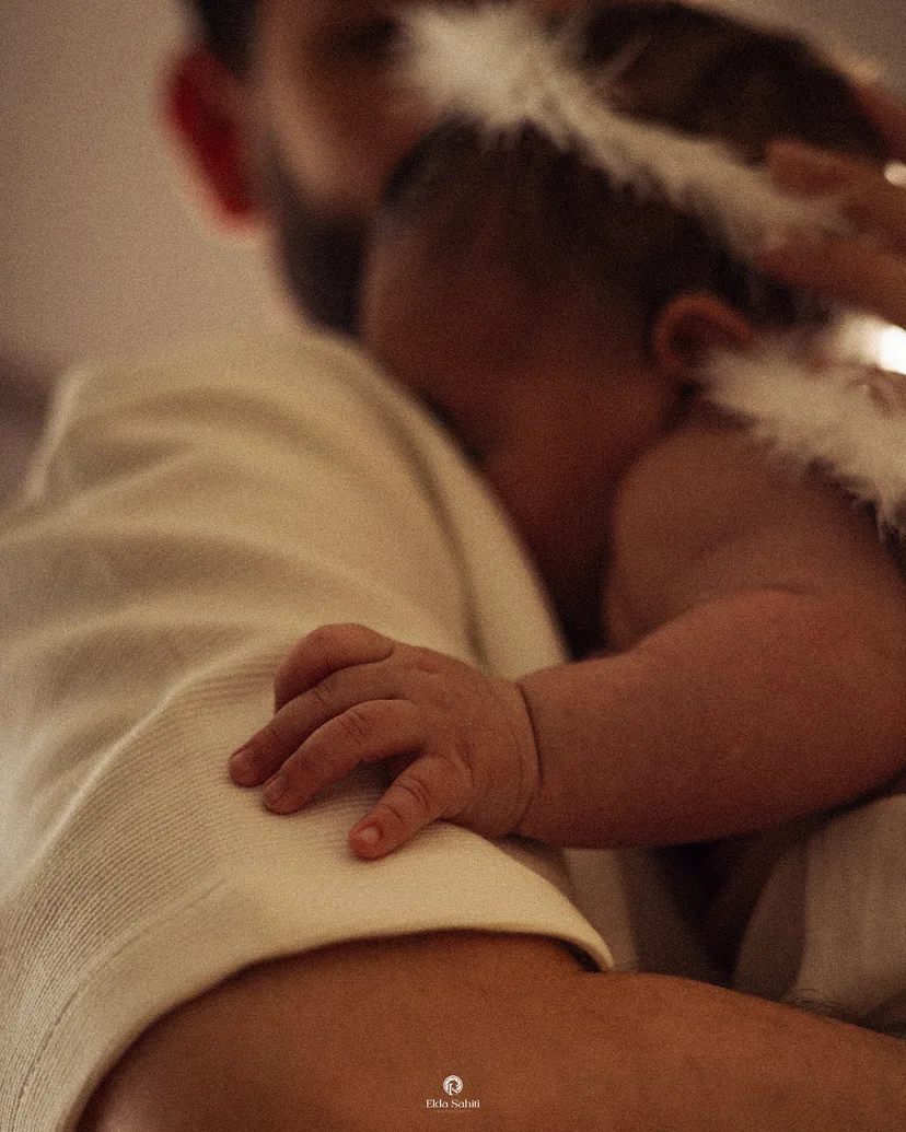 Baby in white feather wings resting a tiny hand on the father's shoulder