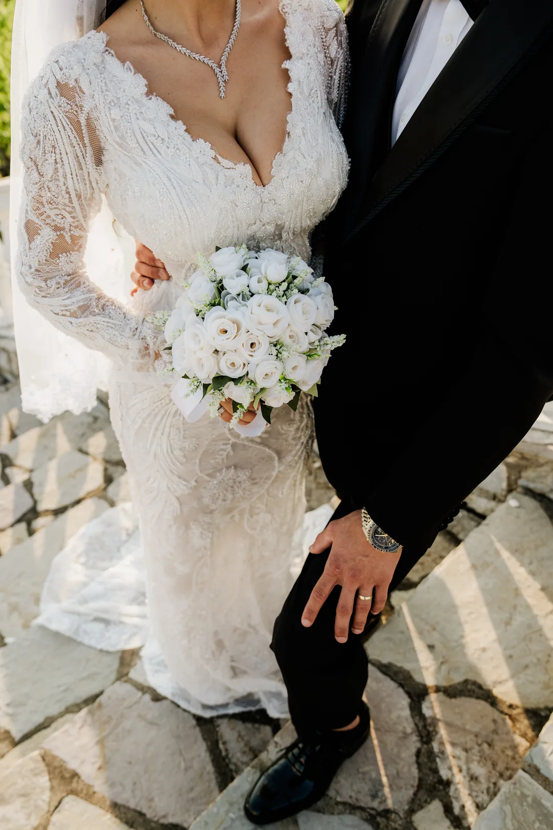 White rose bouquet against her lace gown, the groom's ringed hand at his side