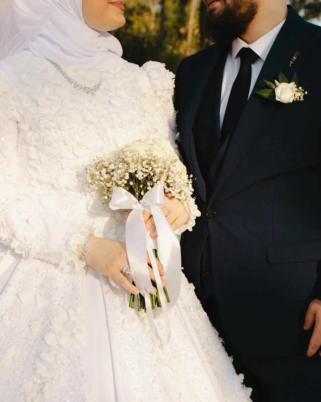Bouquet of small white flowers tied with a satin ribbon, the groom in navy beside her