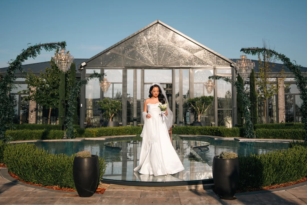 Bride standing by a reflecting pool in front of a glass pavilion