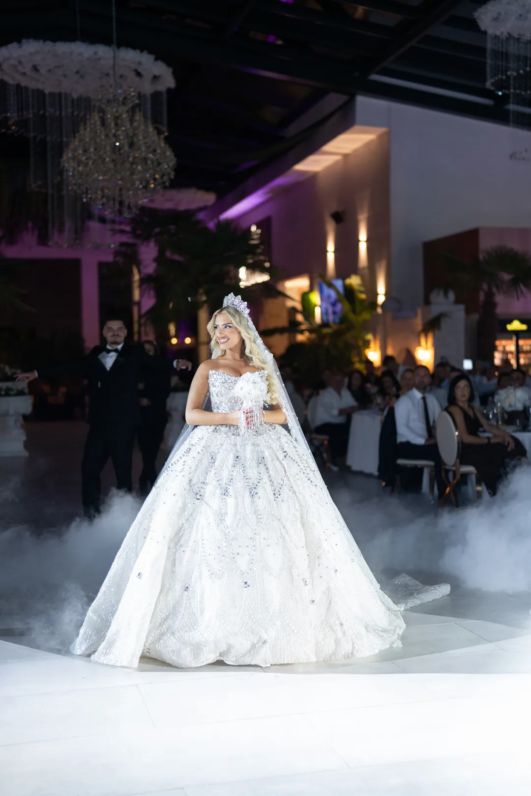 Bride stepping onto the dance floor through low fog, guests at their tables