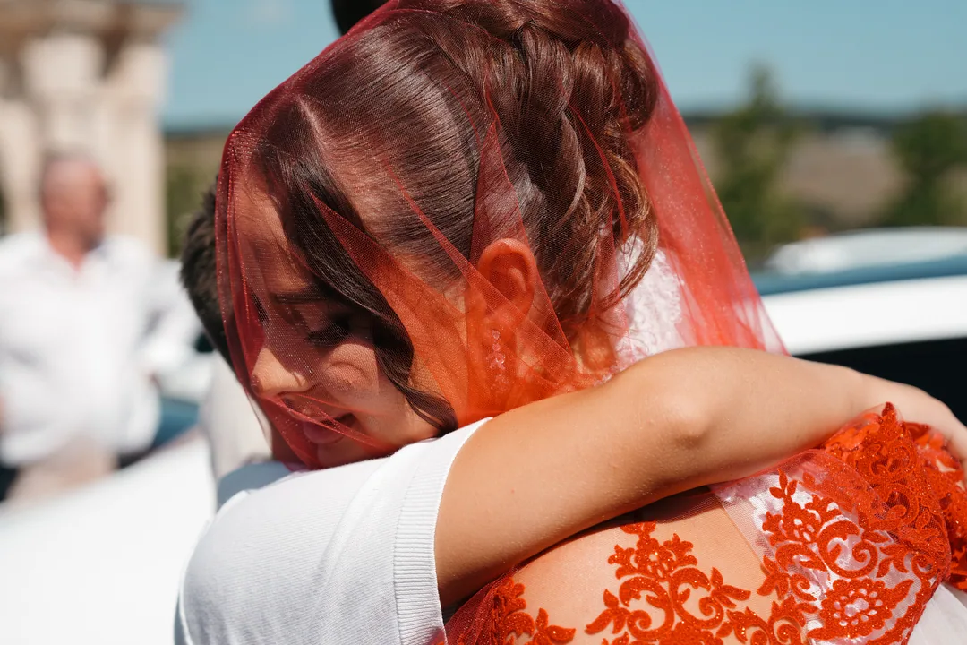 Bride with her eyes closed in an embrace, the red veil falling over her hair