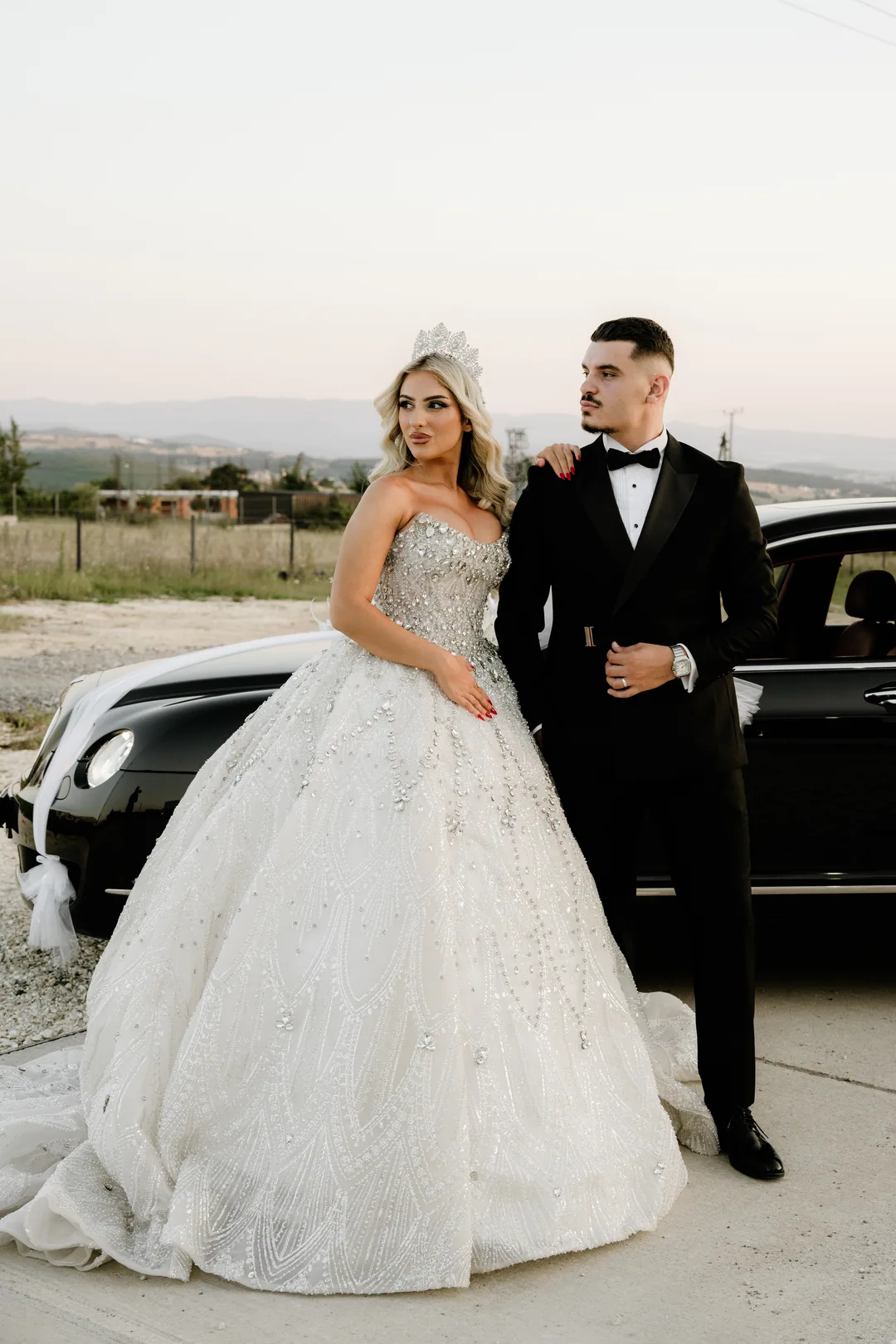 Bride with her hand on the groom's shoulder, the black car behind them