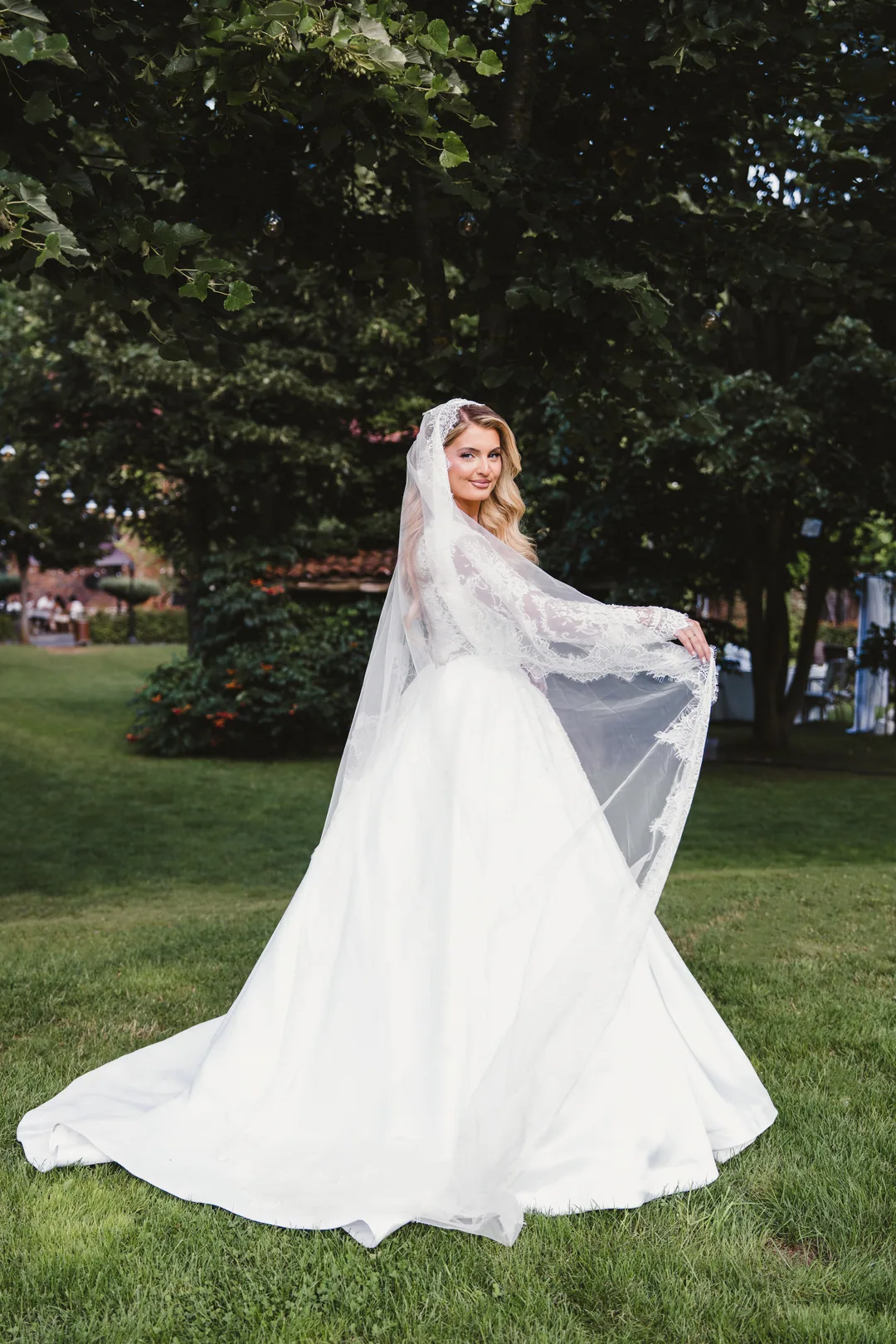 Bride holding out the lace edge of her veil in a garden