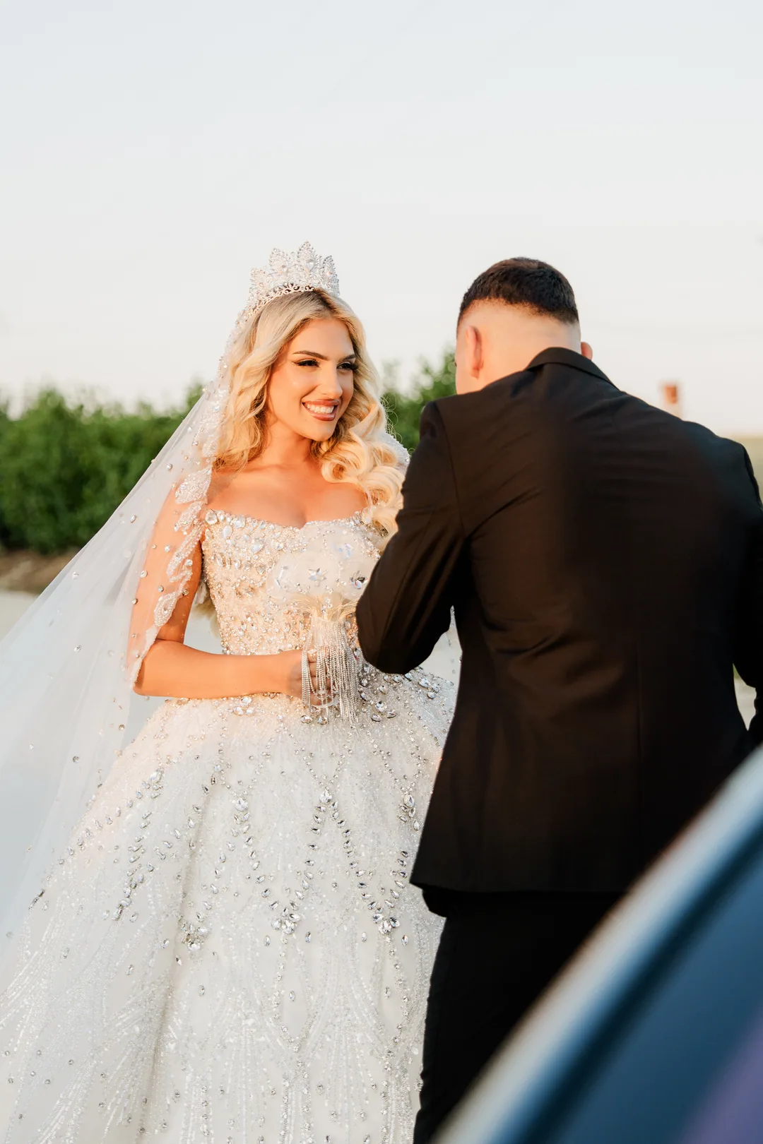 Bride in a crown and crystal gown smiling as the groom takes her arm