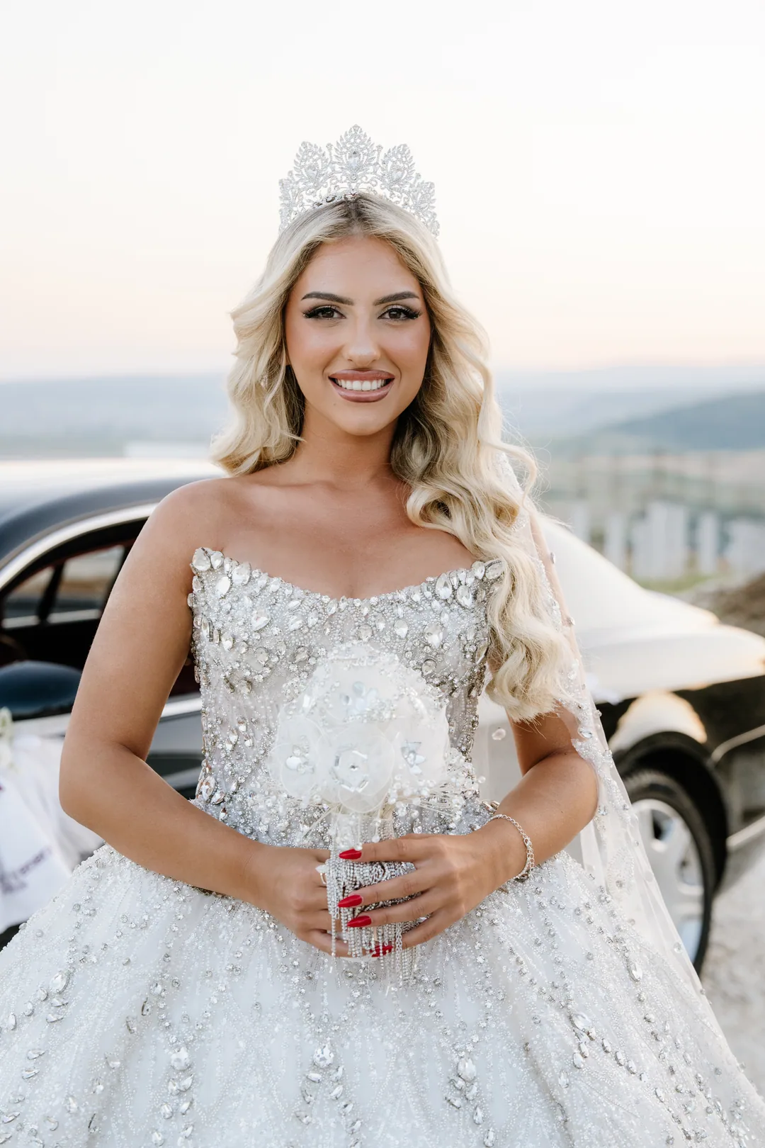 Bride in a crown holding a crystal bouquet, smiling into the camera