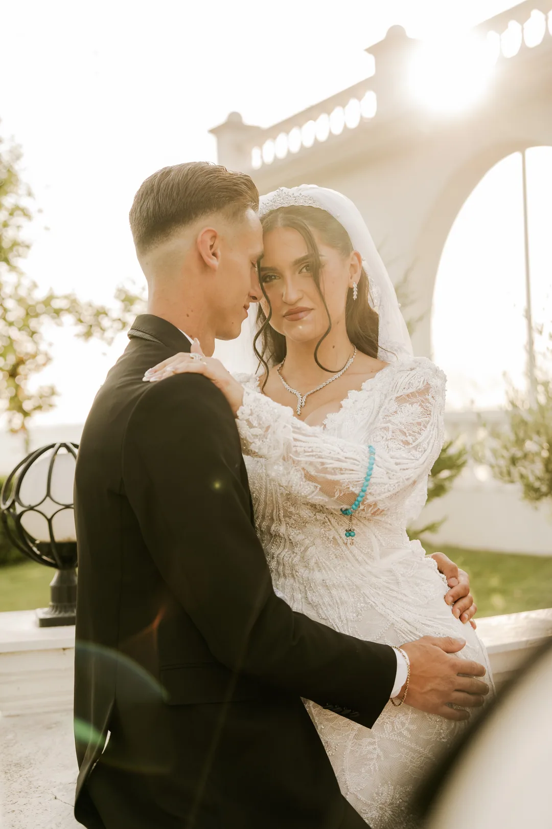 Bride in the groom's arms by white arches, looking into the camera