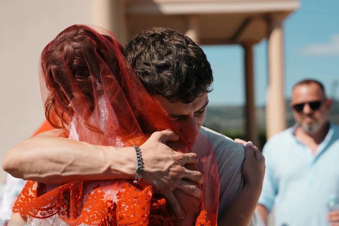 Bride in her red veil in a long hug goodbye