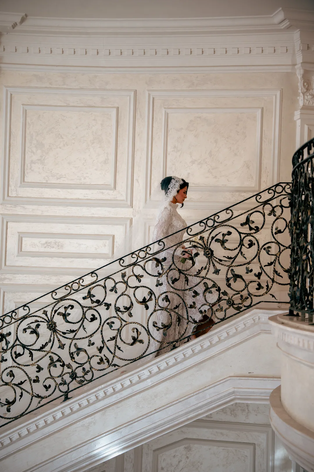 Bride descending a white marble staircase with a wrought-iron railing