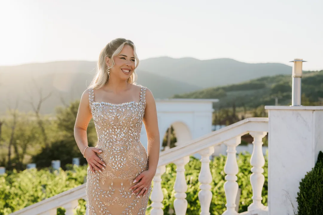 Bride in a champagne beaded dress smiling on the steps above the vineyard, hills beyond