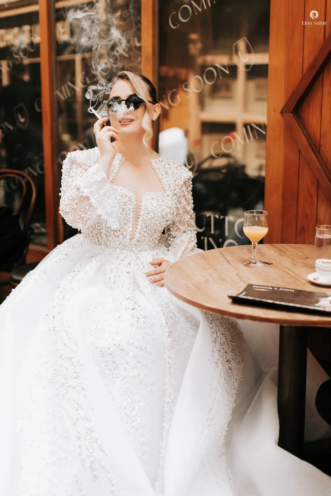 Bride in sunglasses smoking at a café table in her beaded gown