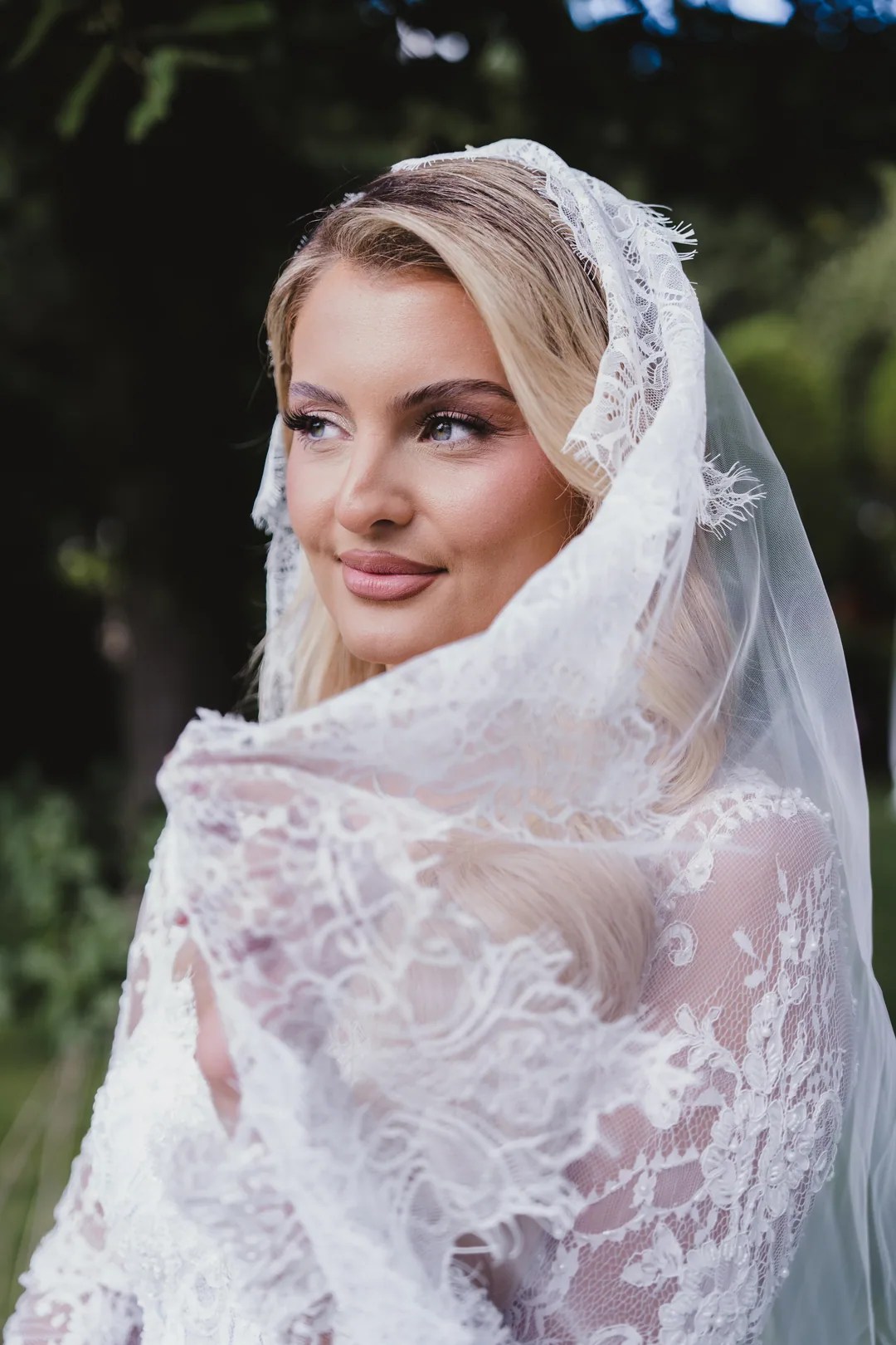 Bride wrapped in her lace veil, glancing to the side with a soft smile