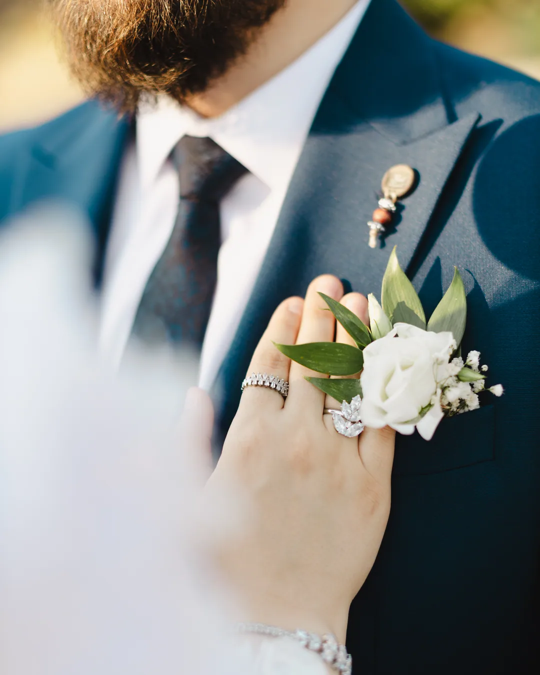 Bride's hand with her rings resting on the groom's lapel beside a white rose