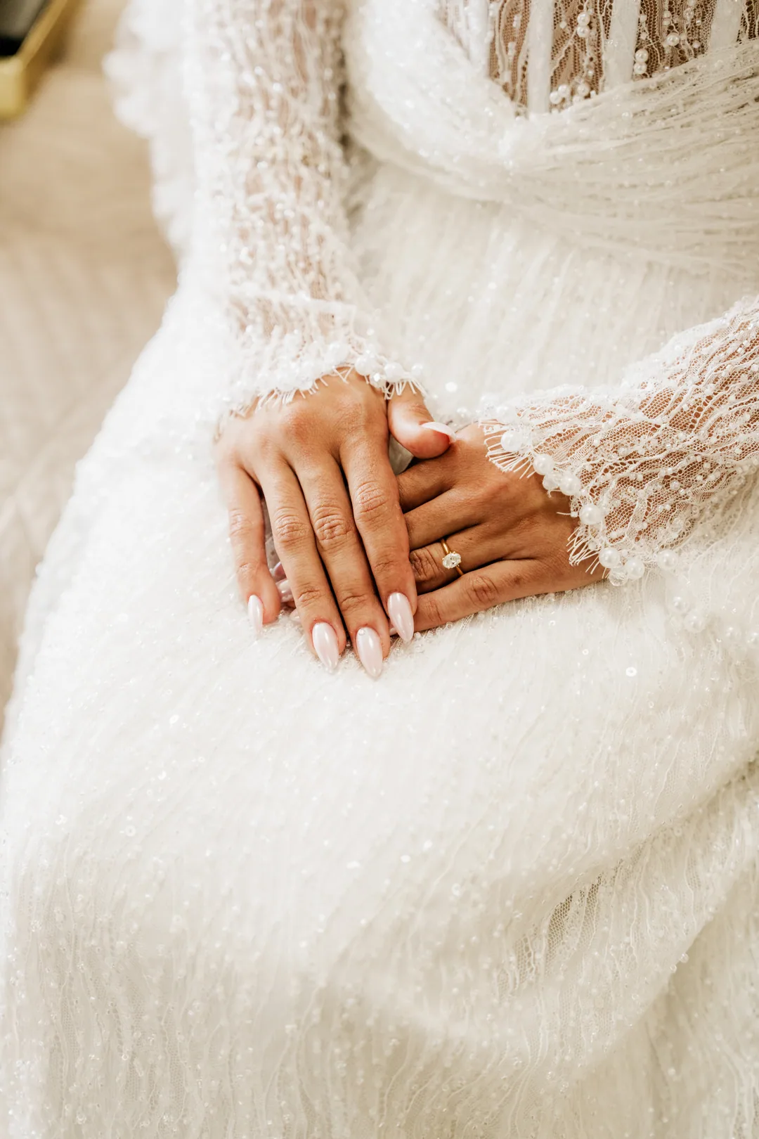 Bride's hands folded on her lace and beaded skirt, the ring on her finger