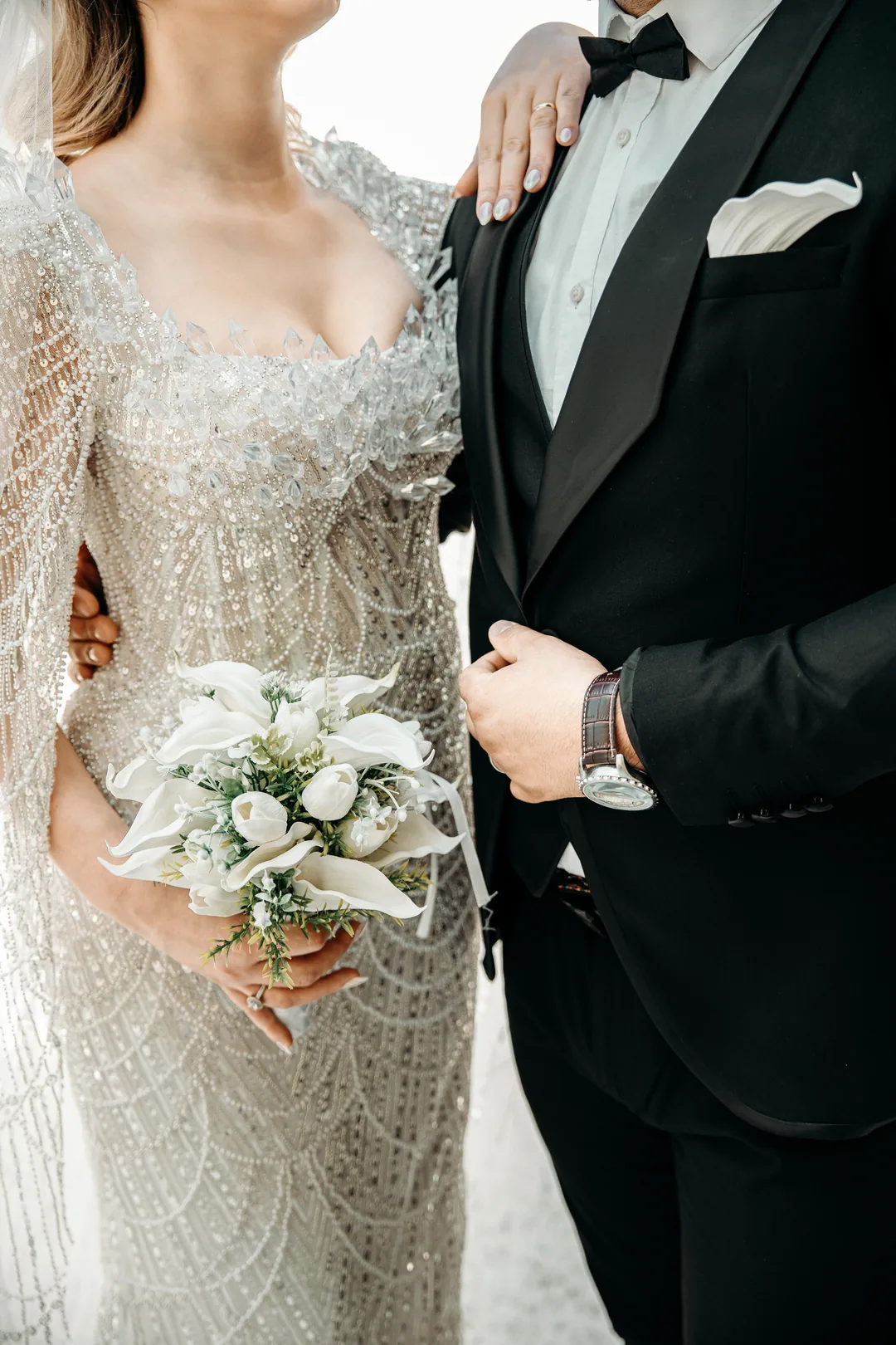 White calla bouquet against her beaded gown, the groom's arm around her waist