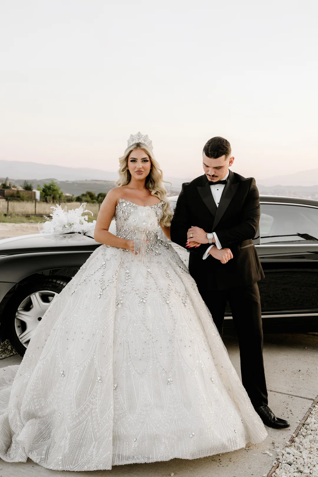 Bride and groom arm in arm in front of a black car
