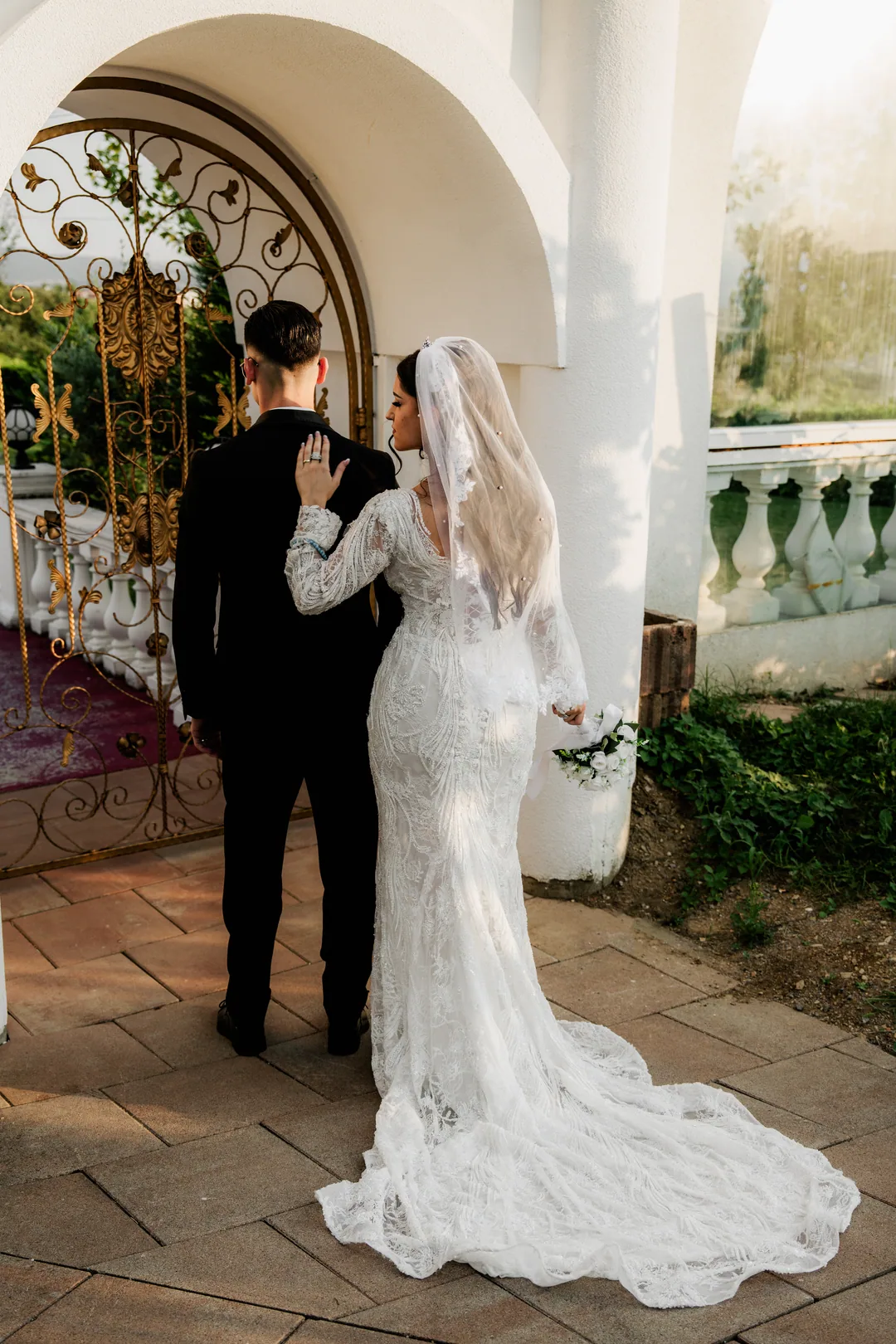 Couple from behind at an ornate arched gateway, the bride glancing back