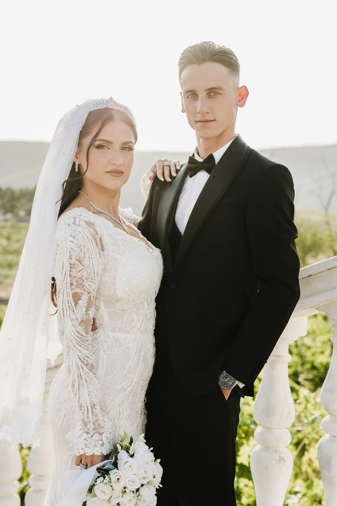 Couple at a white balustrade, his arm around her, white roses in her hand