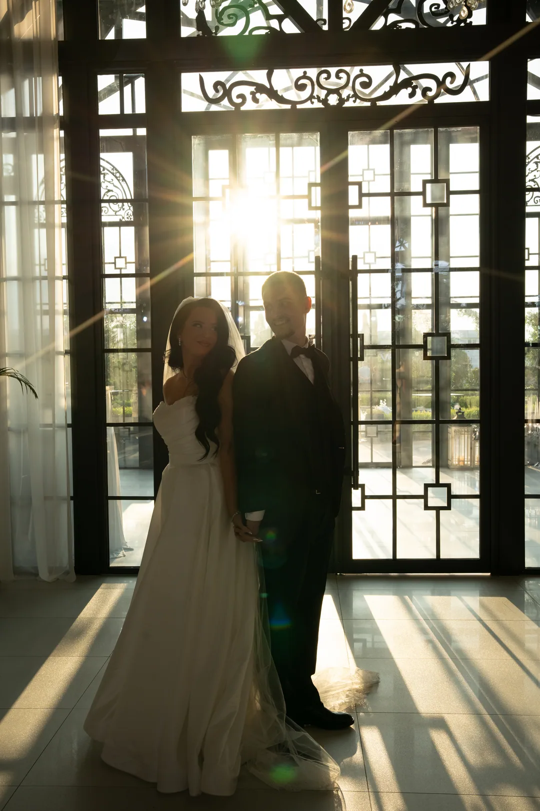 Couple back to back as the sun bursts through the ironwork of the doors