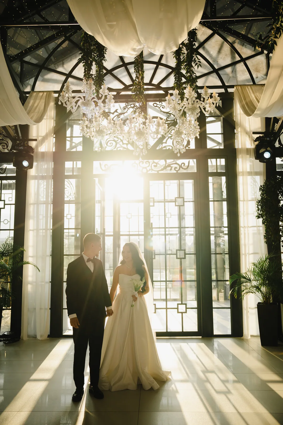 Couple standing before the wrought-iron glass doors, backlit by the afternoon sun