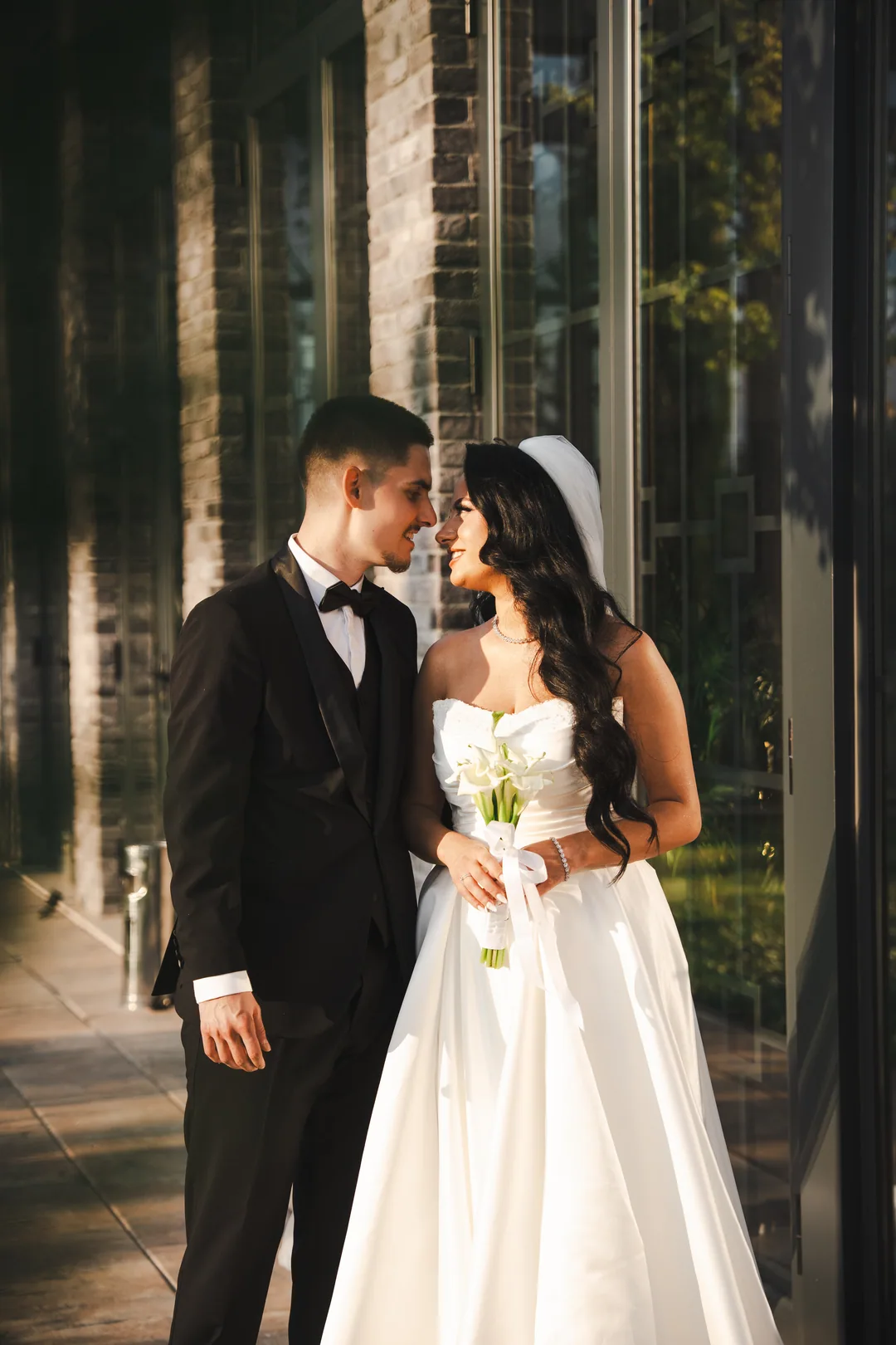 Couple close together in the shade of the pavilion, calla lilies in her hands
