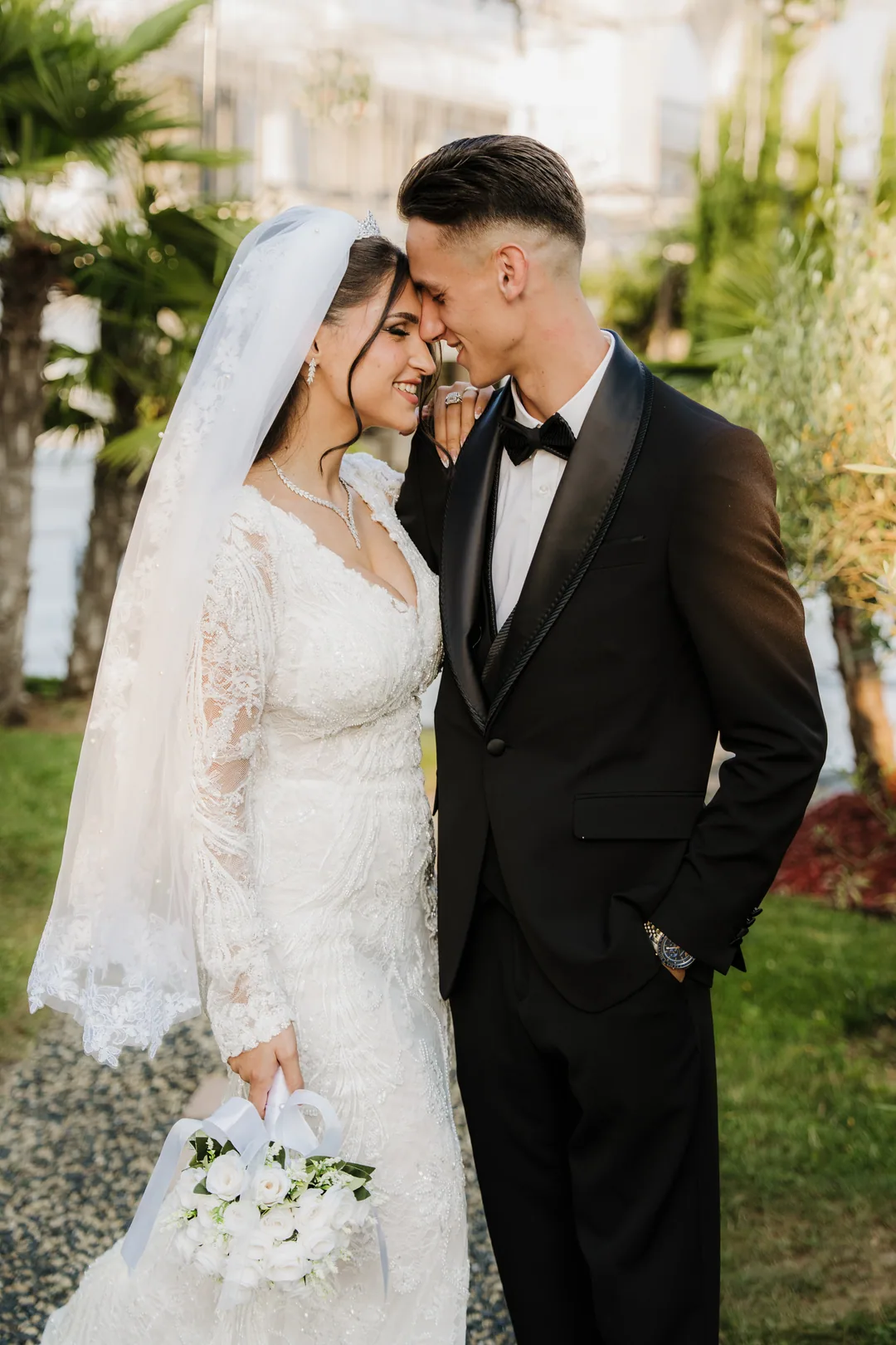Couple forehead to forehead in the garden, smiling, her bouquet at her side