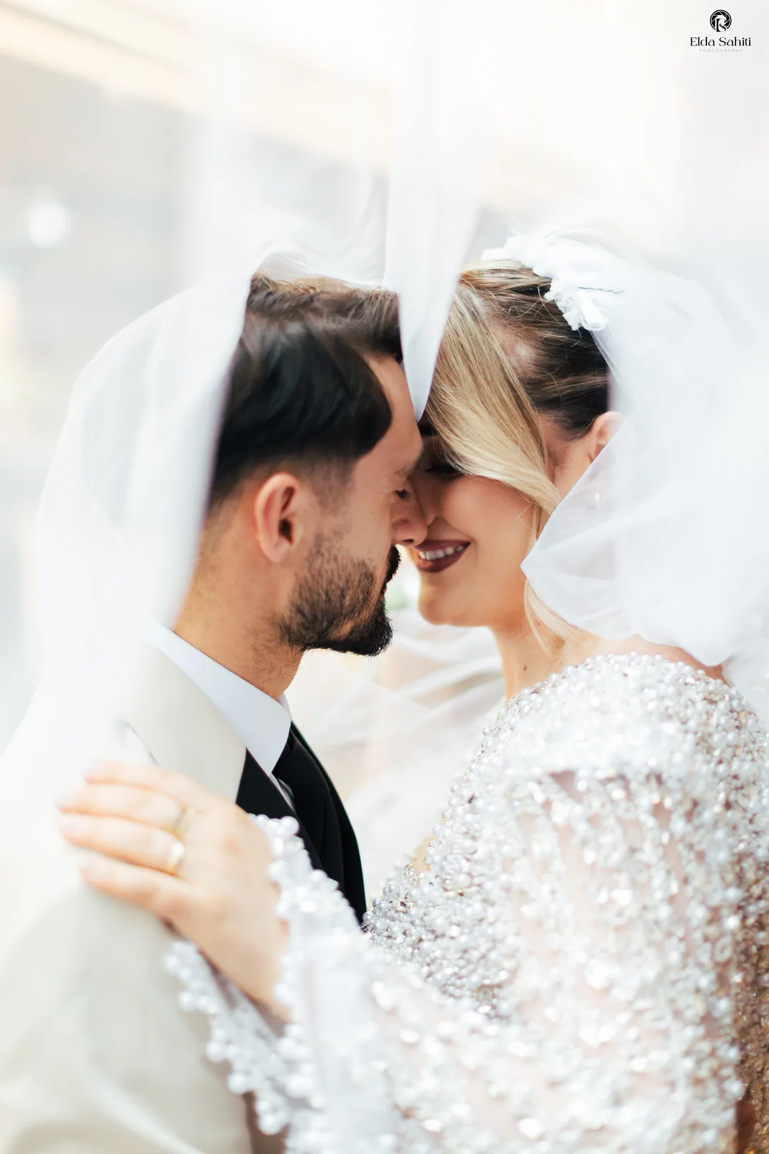 Couple forehead to forehead beneath her veil, pearls on her sleeves