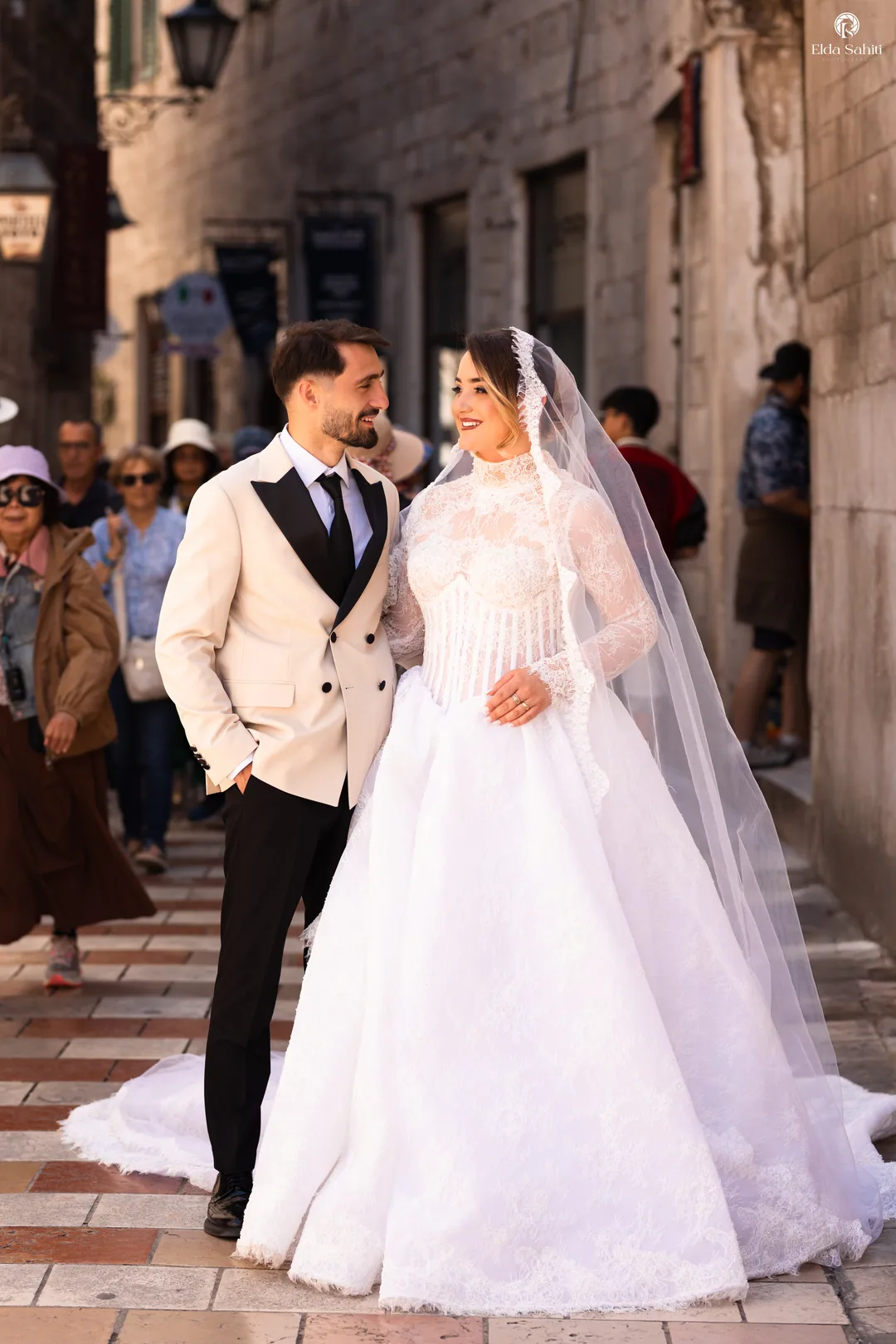 Couple in a busy old-town street, the groom in a cream double-breasted jacket