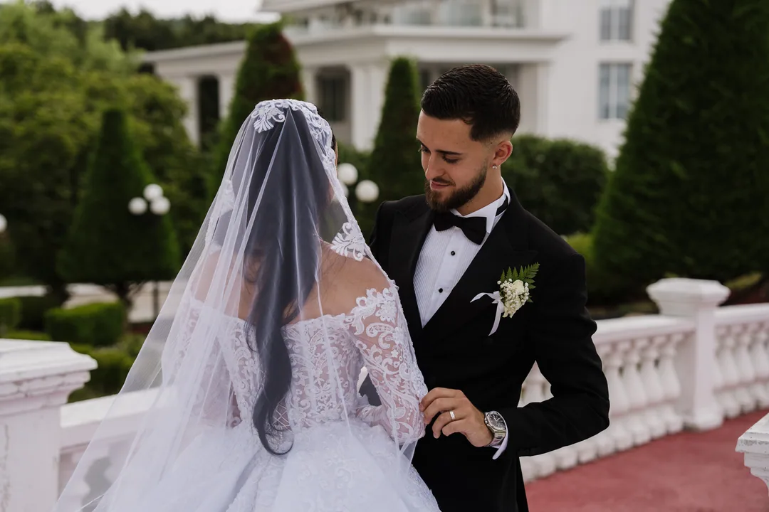 Bride under a lace veil and the groom in the palace garden, clipped cypresses behind