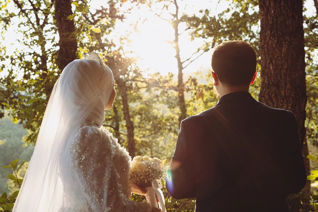 Bride and groom seen from behind in a pine forest at golden hour