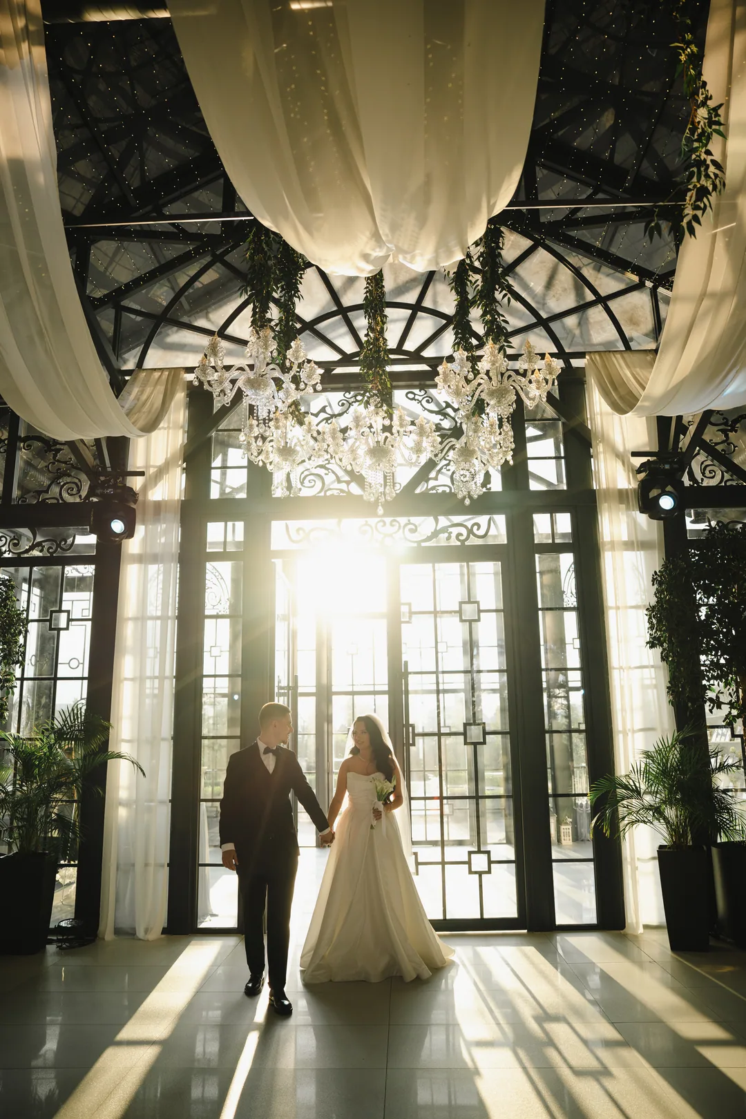 Bride and groom in the sunbeams beneath a draped ceiling and chandelier