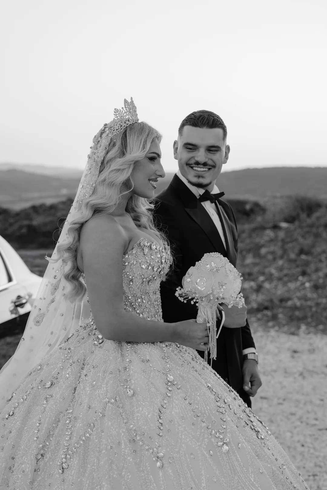 Bride and groom laughing side by side, a crystal bouquet in her hand, in black and white