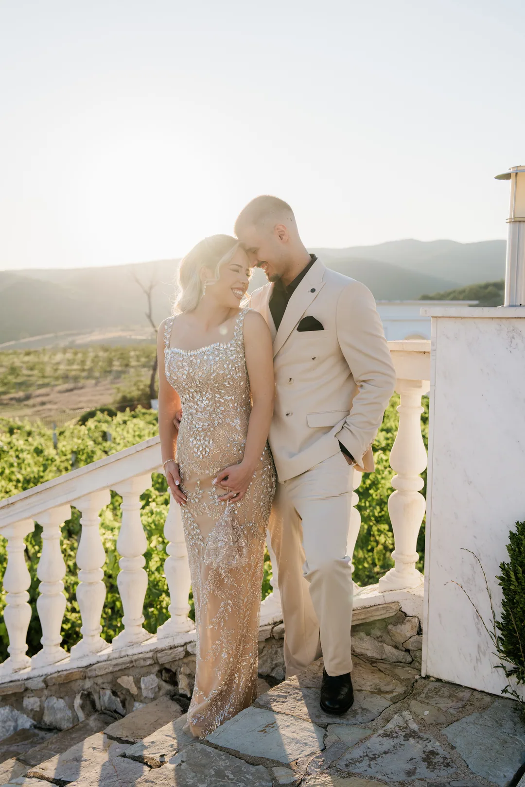 Couple leaning together on white balustrade steps above the vineyard at sunset