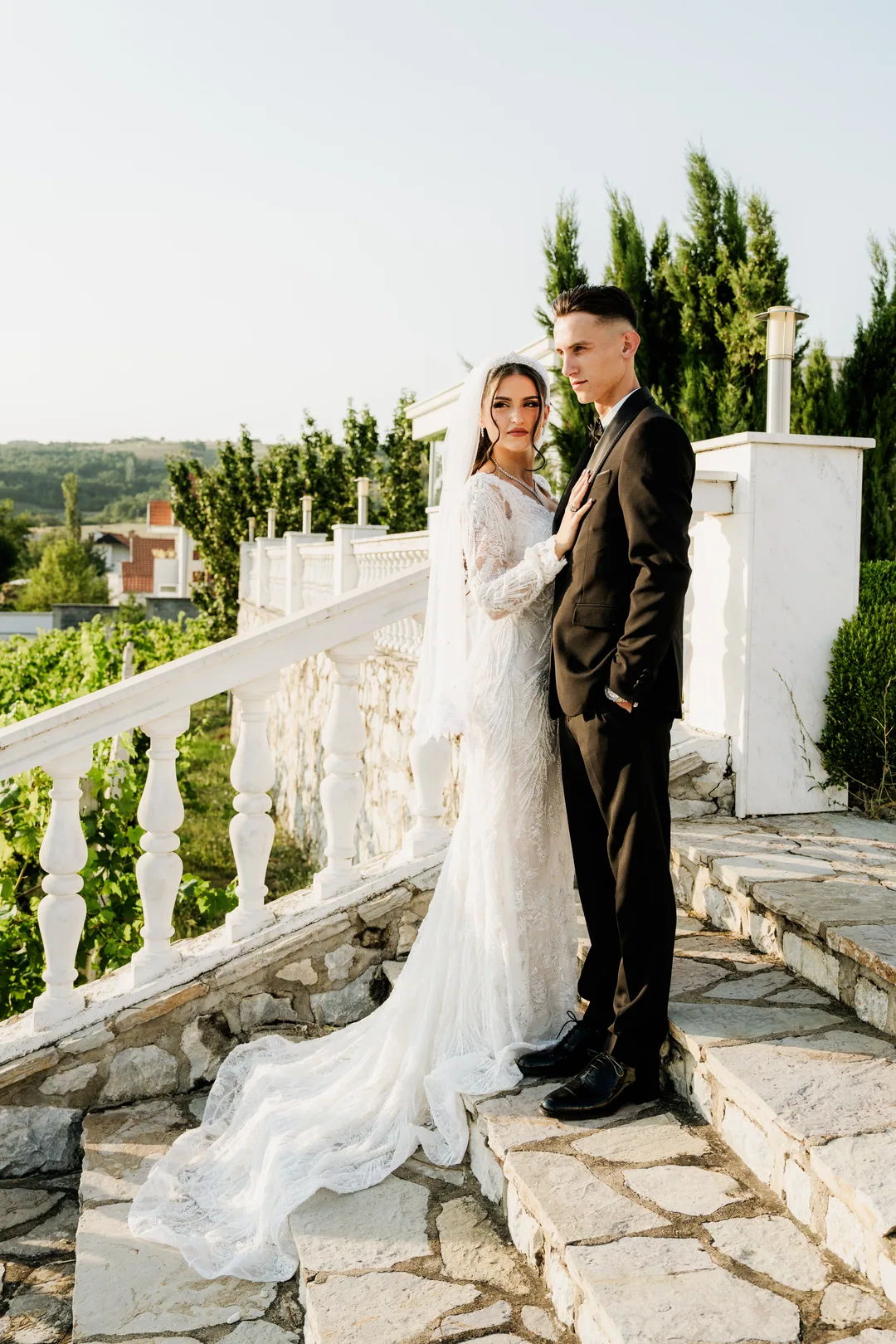 Bride and groom on the steps looking into the camera, cypresses behind