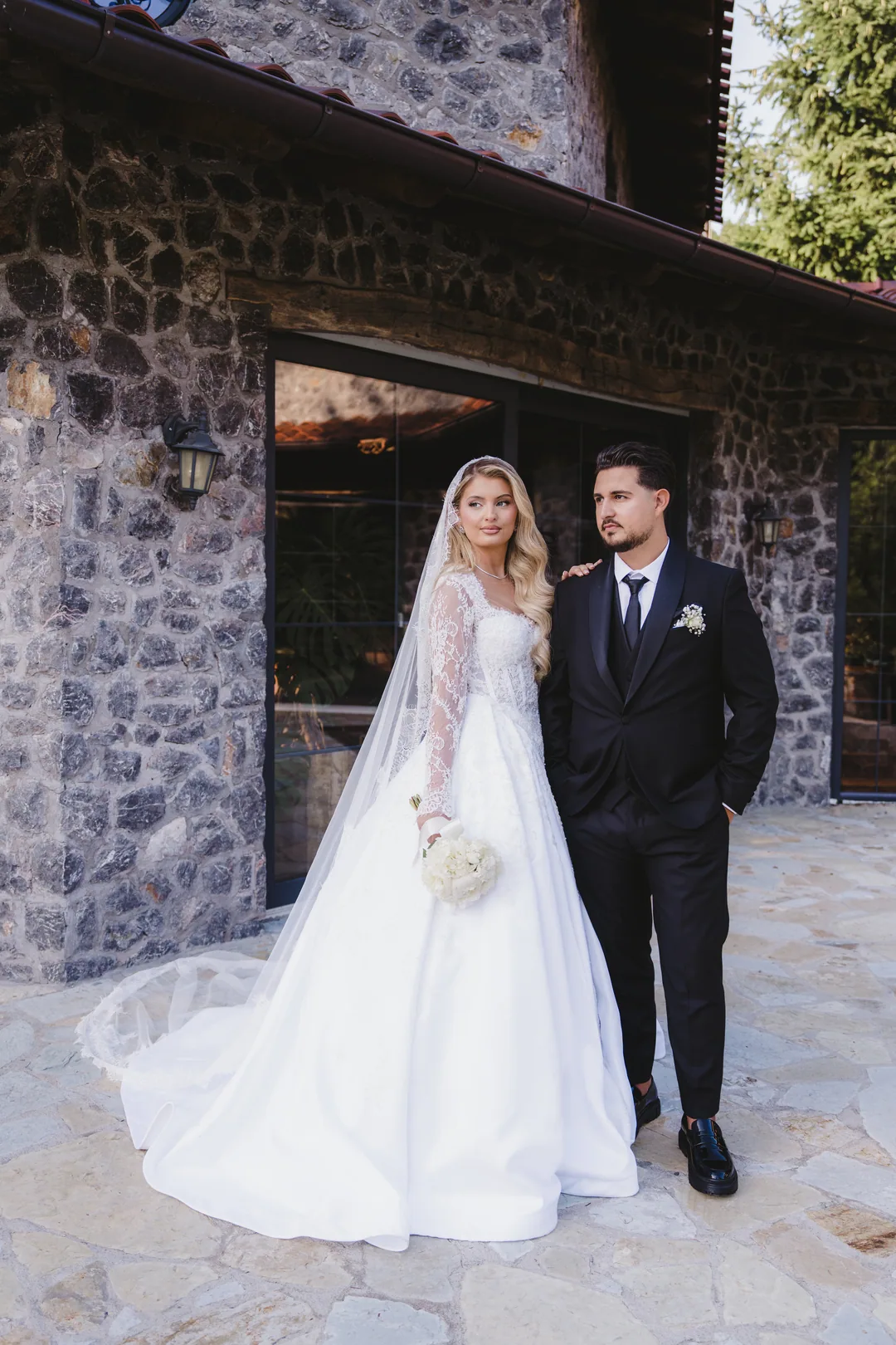 Bride and groom on the stone terrace of the house, her train behind her