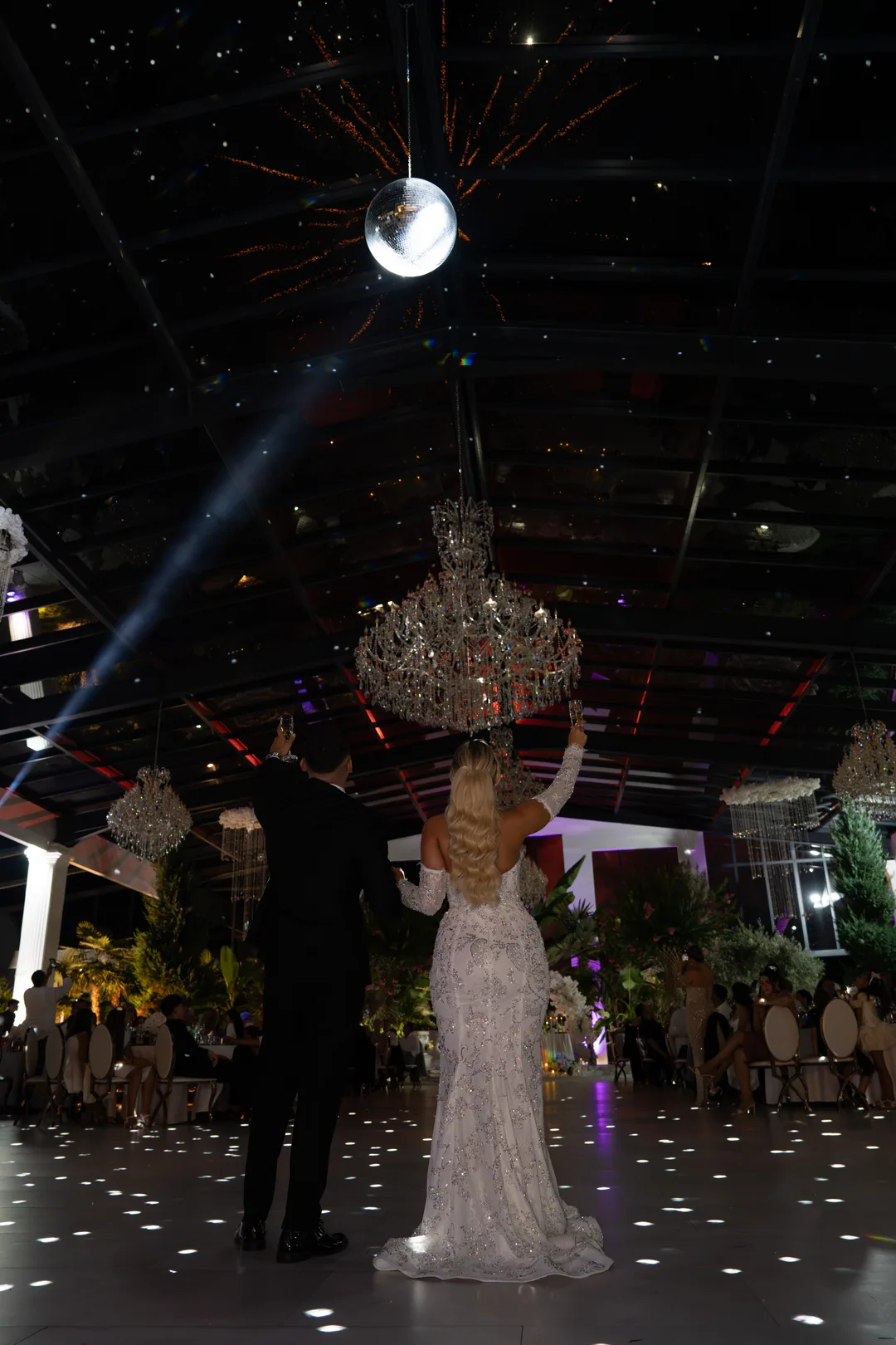 Bride and groom raising their hands to the guests beneath the chandelier