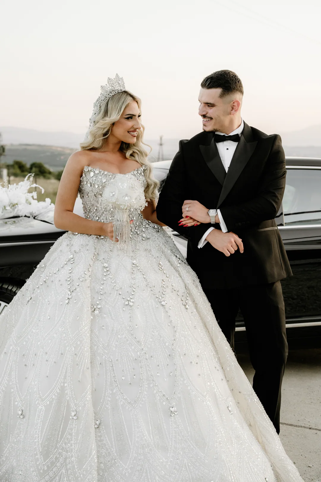 Bride and groom smiling at each other beside the car