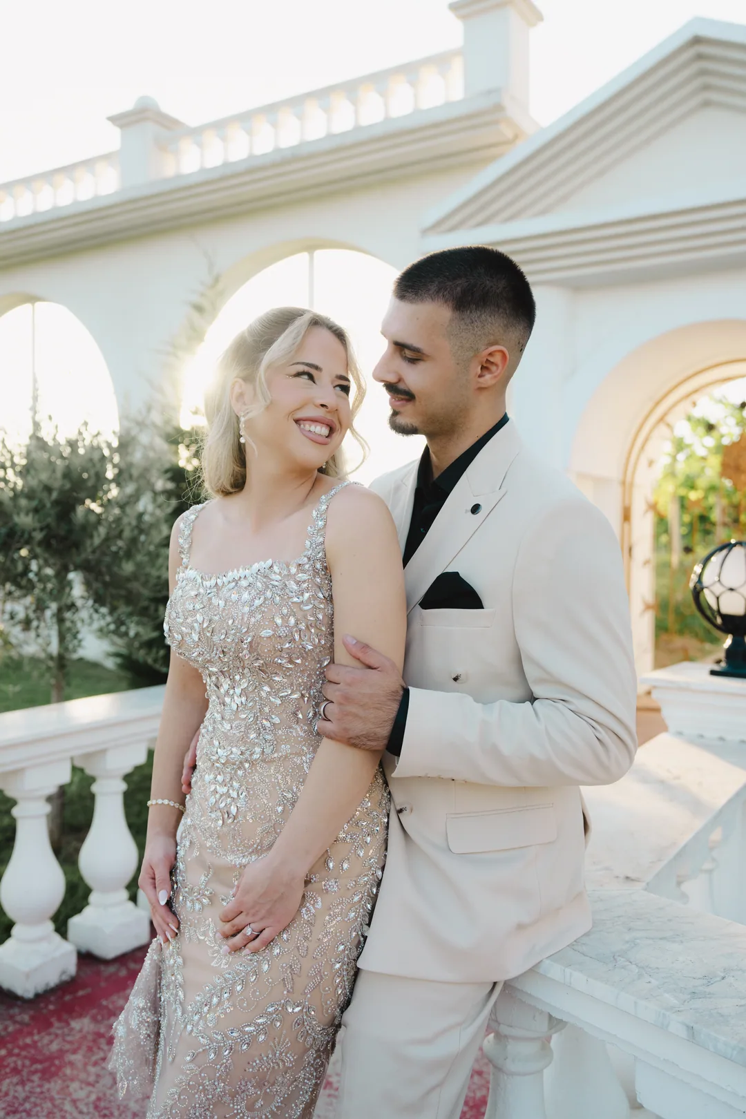 Couple smiling at each other by white arches, her gown sparkling