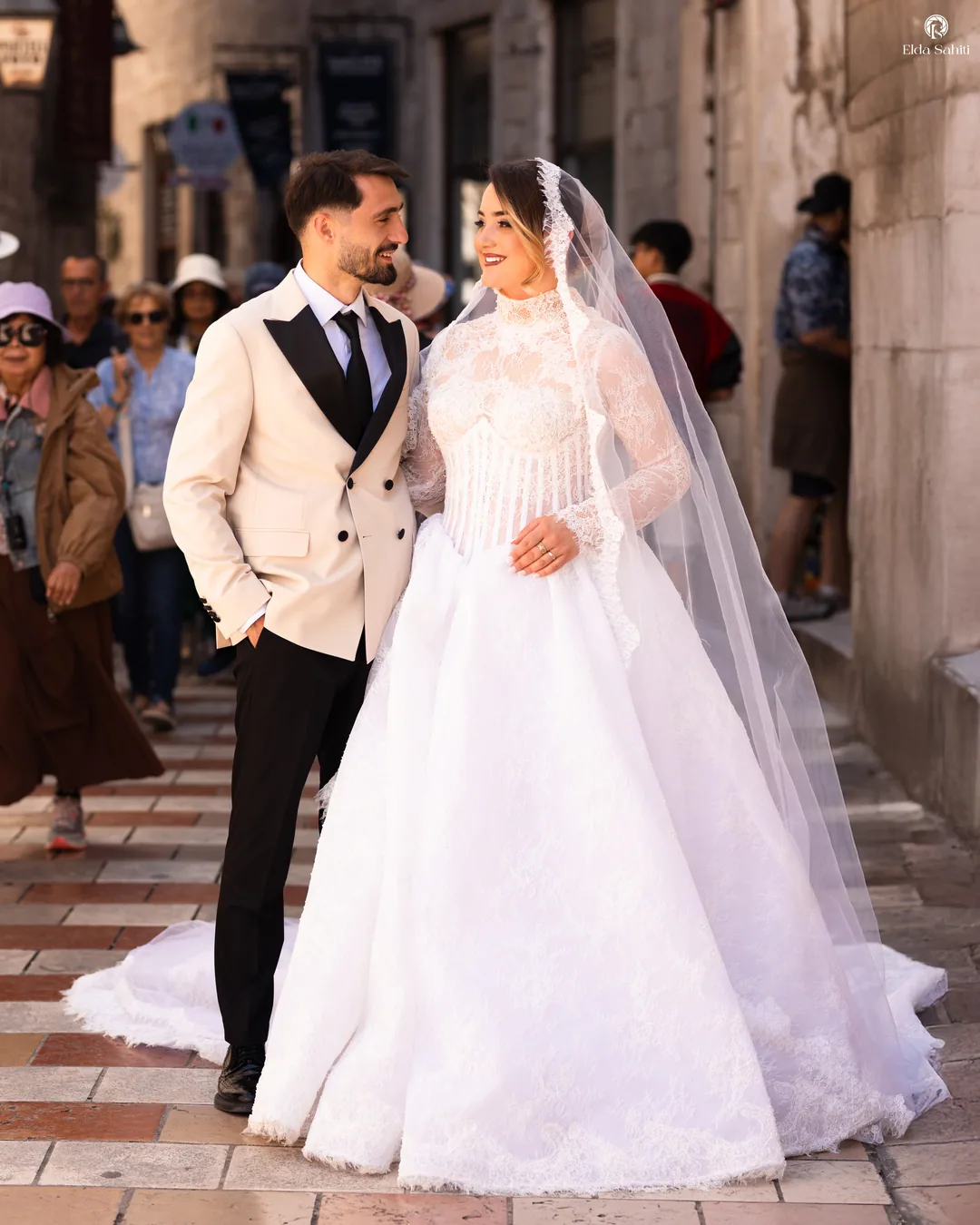 Bride and groom smiling in the old town, tourists passing behind them
