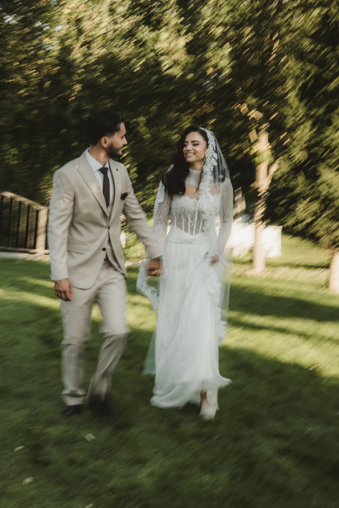 Couple walking hand in hand across a lawn, the trees blurred with movement
