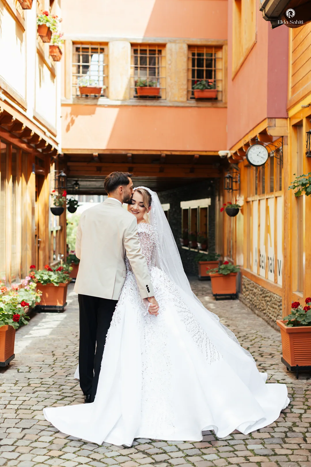 Couple walking down a cobbled lane between wooden houses, the bride looking back