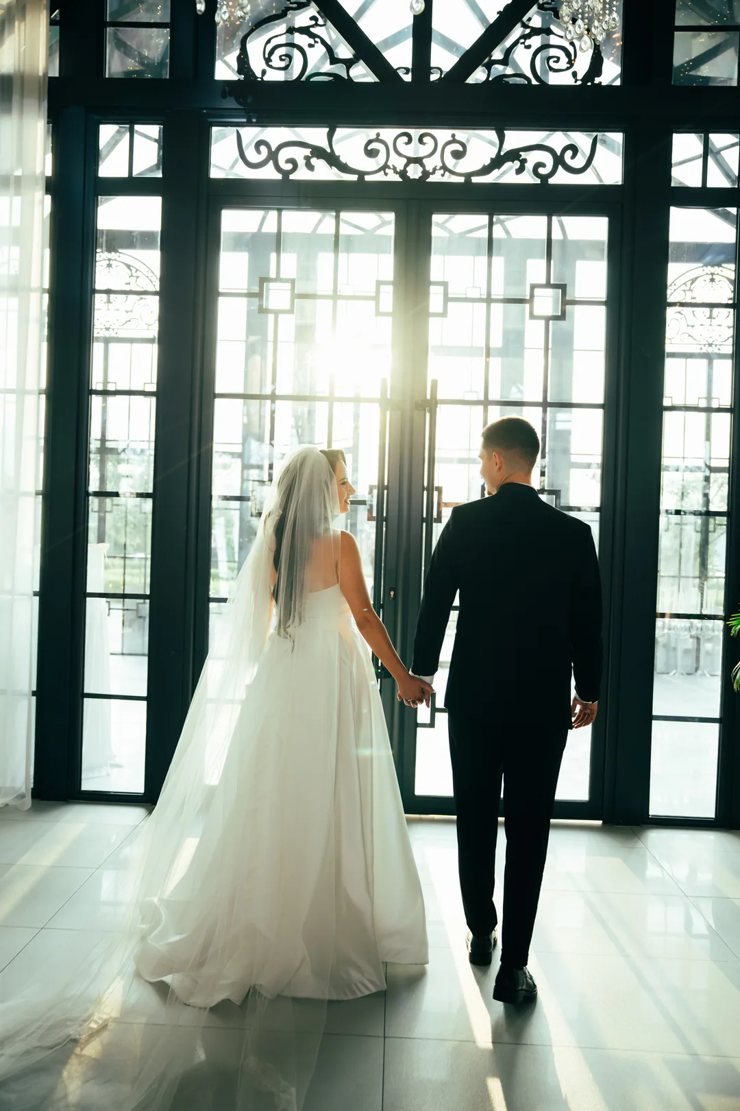 Couple walking hand in hand towards the tall sunlit doors