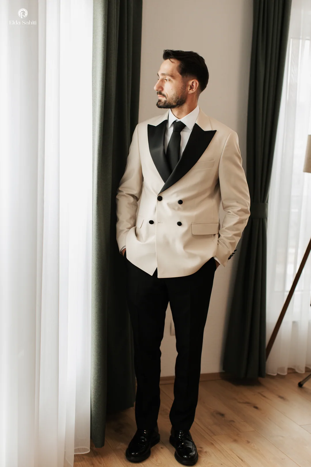 Groom in a cream double-breasted tuxedo looking out of the window