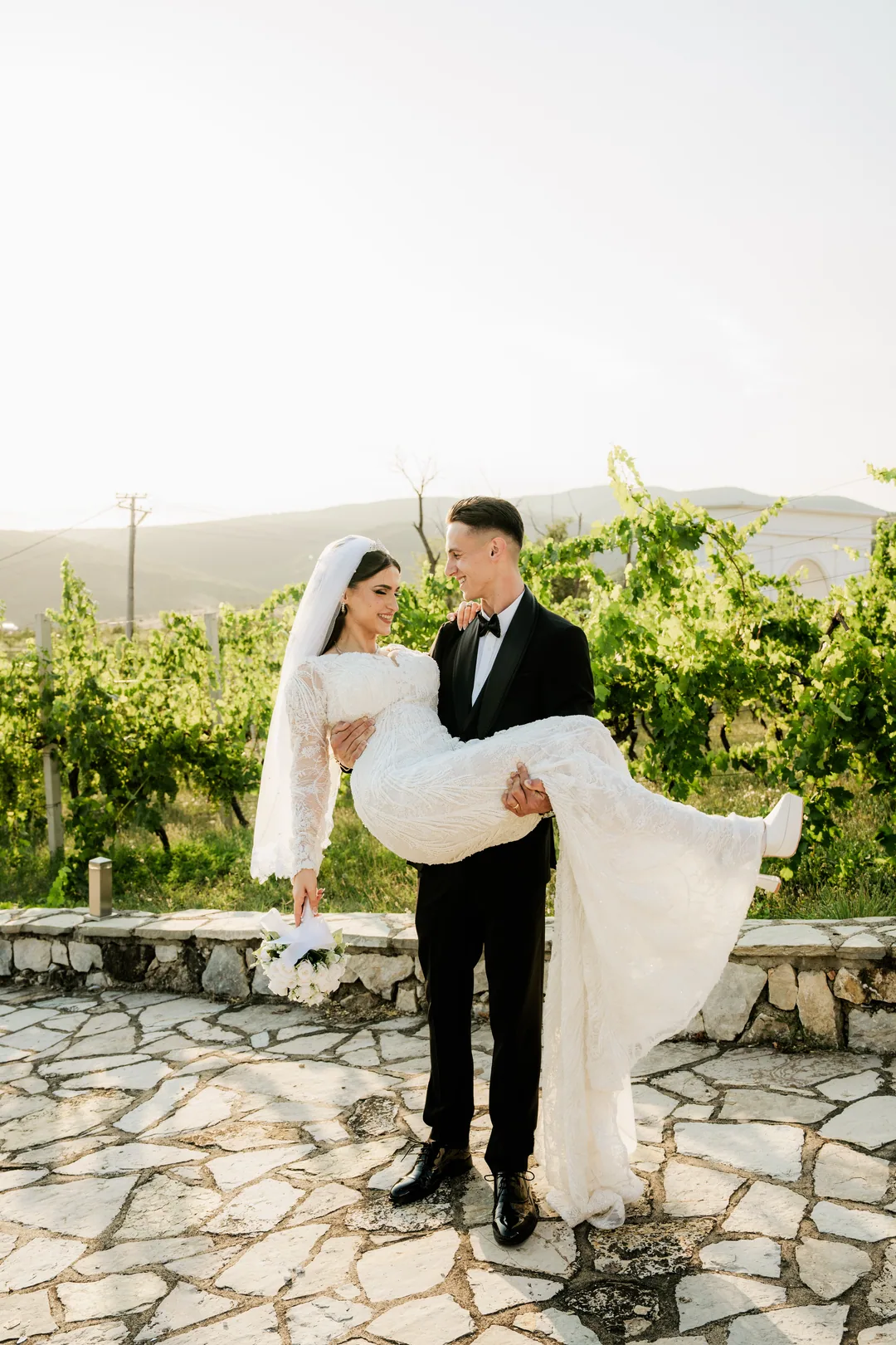 Groom carrying the bride in his arms in front of the vineyard
