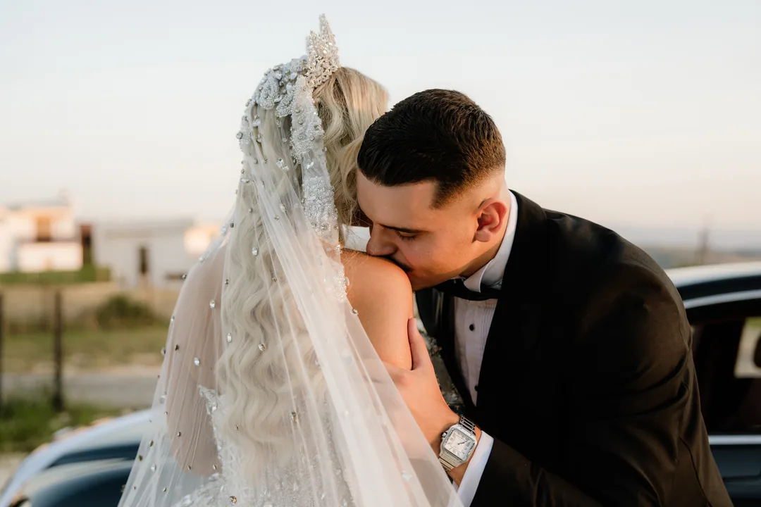 Groom kissing the bride's shoulder through her crystal veil at sunset