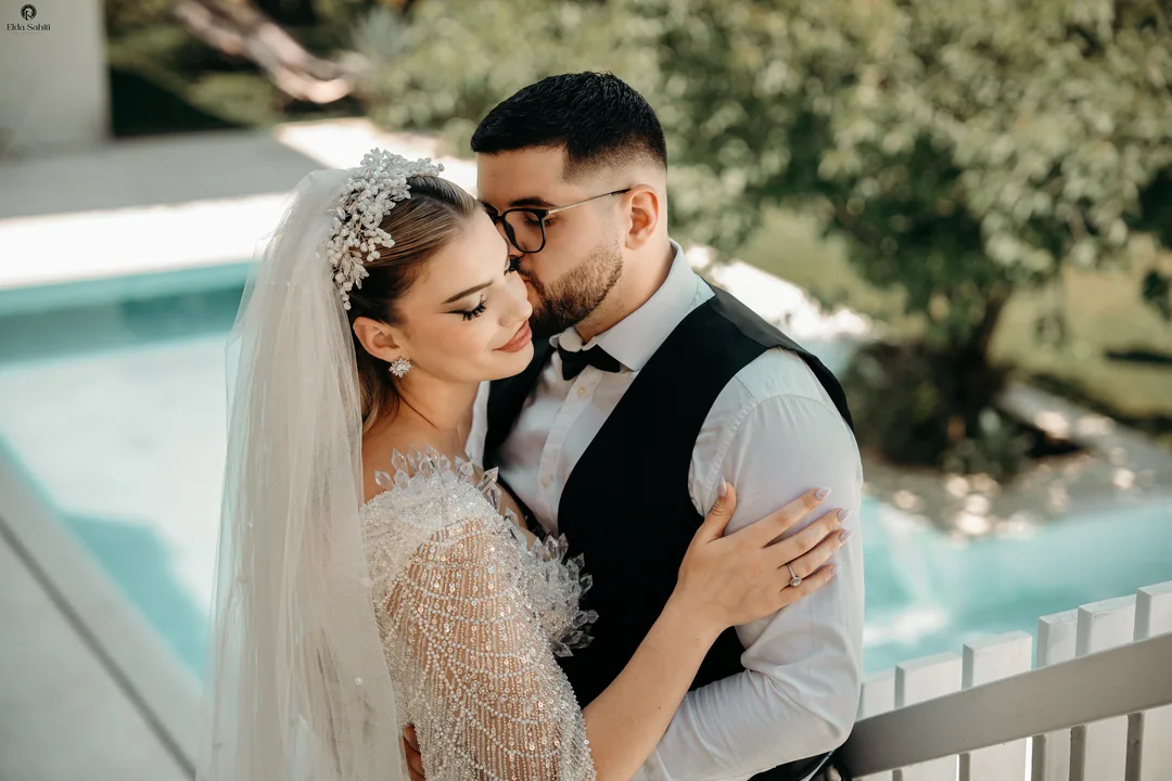 Groom kissing the bride's temple by the pool, her eyes closed