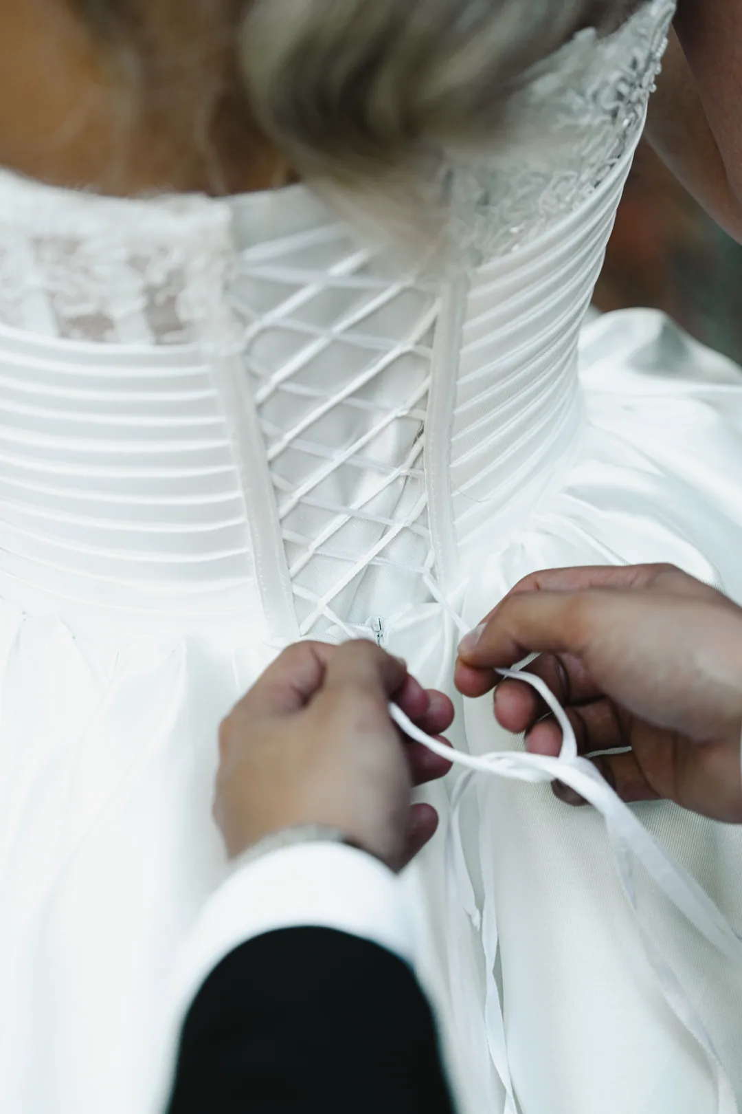 Groom tying the corset laces at the back of the bride's gown