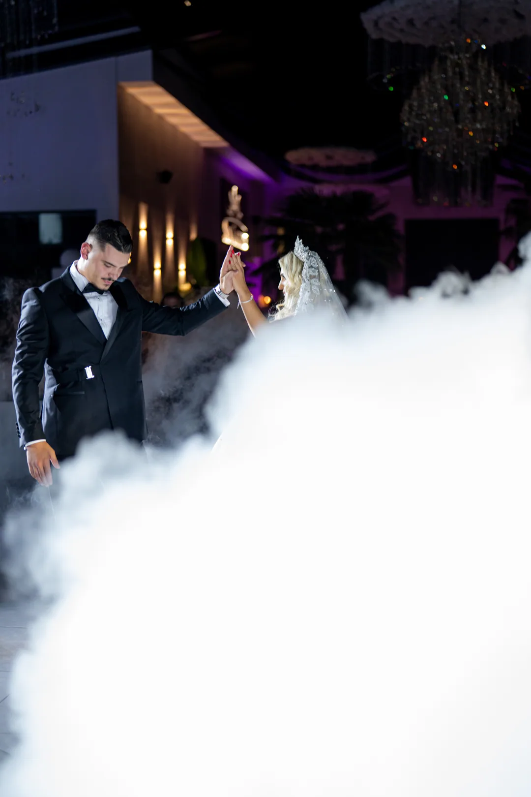 Groom leading the bride through thick fog under purple lights
