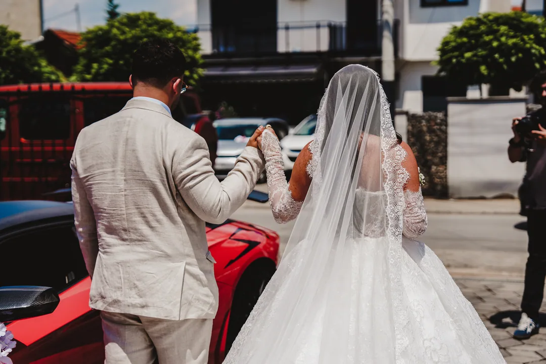 Groom leading the bride by the hand towards a red sports car in the street